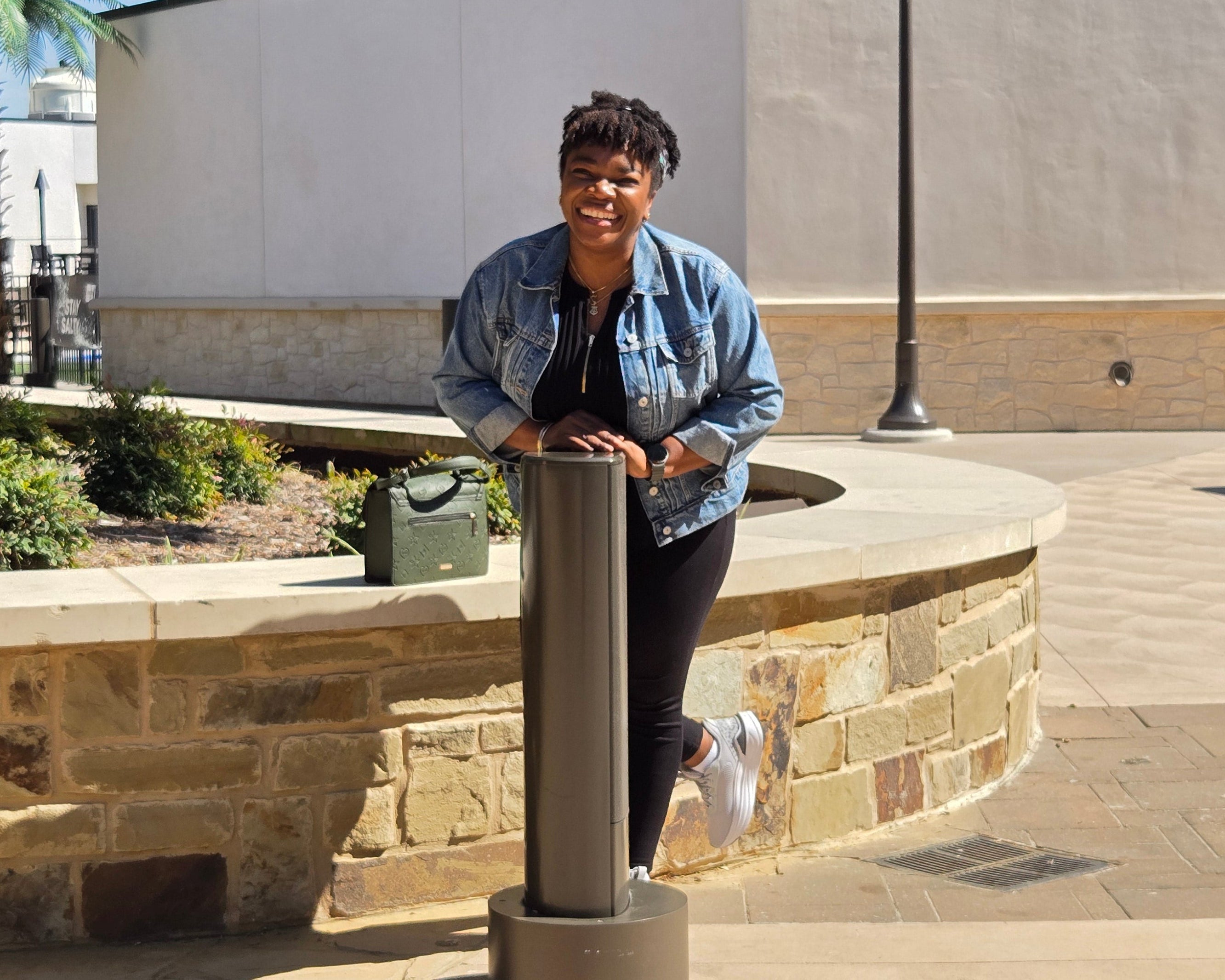 Person standing outdoors near a building with palm trees in the background